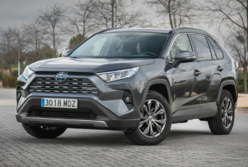 Un SUV Toyota gris estacionado en una superficie pavimentada con árboles al fondo.
