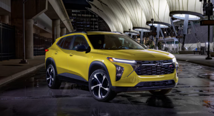 SUV amarillo estacionado de noche bajo un moderno toldo, con el pavimento mojado reflejando las luces.
