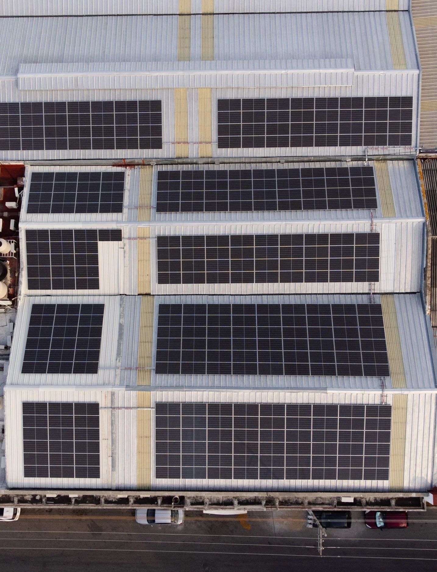 Vista aérea del tejado de un almacén cubierto con múltiples paneles solares a lo largo de una calle.