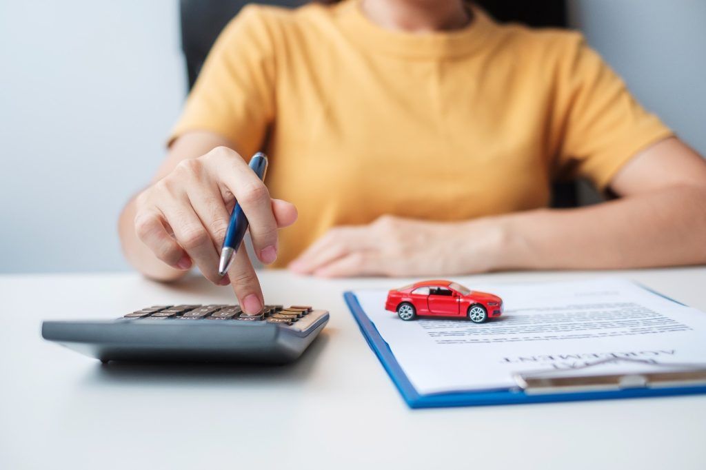 Persona usando una calculadora junto a un coche de juguete y papeles sobre un escritorio.