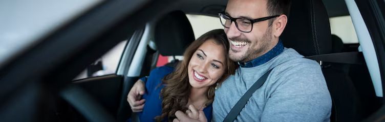 Una pareja sonriente sentada en un coche se toma una selfie.