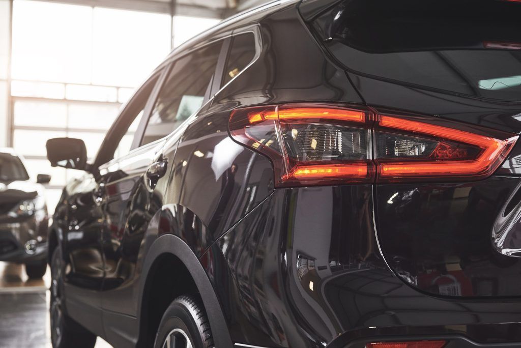 Un SUV negro estacionado en el interior de una sala de exposición o garaje, con las luces traseras encendidas.