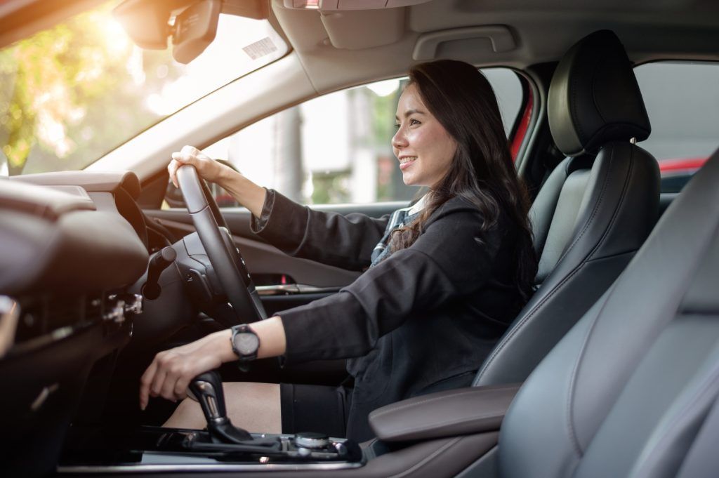 Mujer sentada en el asiento del conductor de un coche, sonriendo y sujetando el volante.
