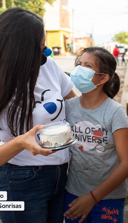 Voluntarios enmascarados entregan un recipiente de comida a un niño en la calle.