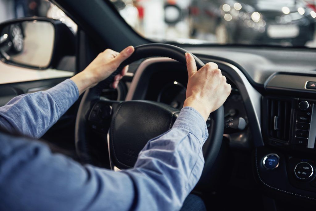 Manos agarrando el volante dentro de un coche, conduciendo por una carretera.