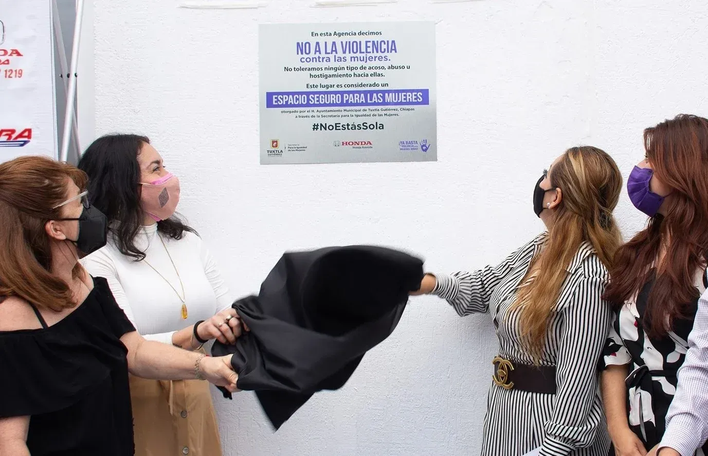 Cuatro mujeres develando una placa en la pared durante una ceremonia, sosteniendo una tela negra frente a ella.