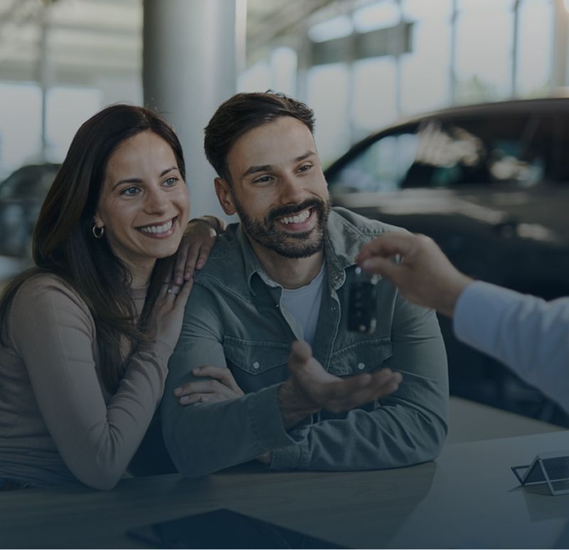 Pareja sonriente conversando con un vendedor de autos en la sala de exposición de un concesionario.