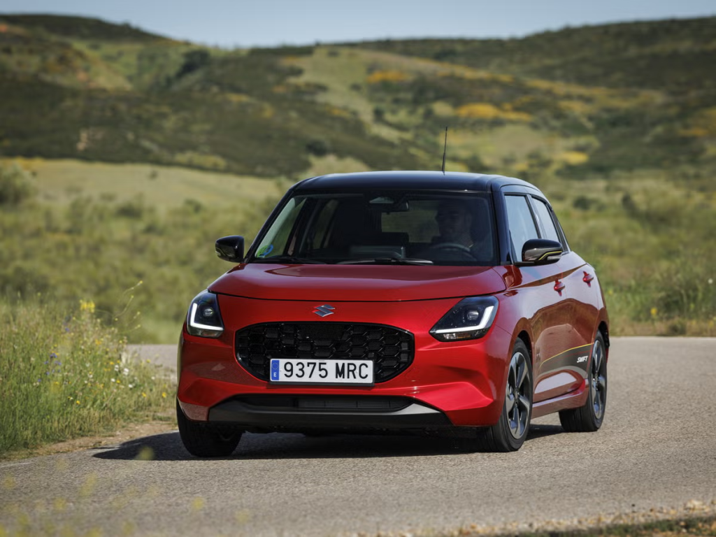 Un SUV compacto rojo circula por una carretera rural con colinas al fondo.