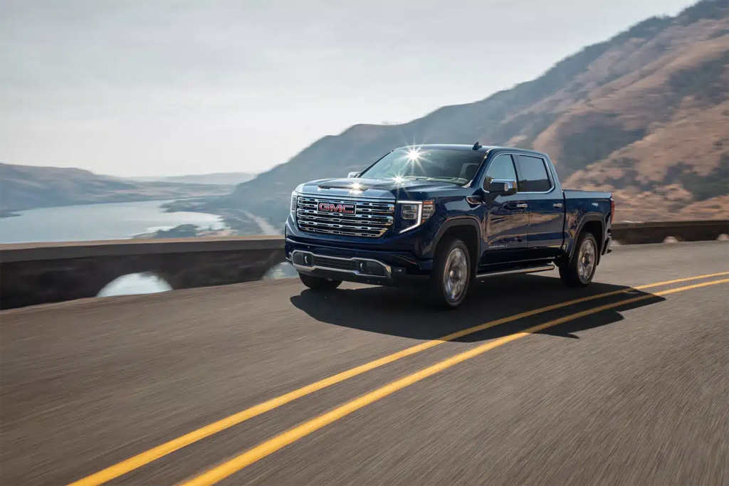Camioneta azul circulando por una carretera de montaña con vistas al océano al fondo.