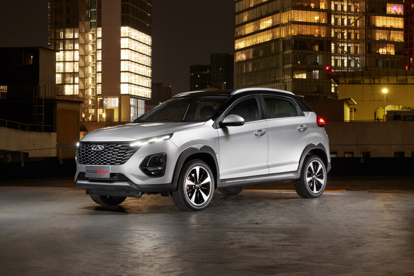 Un SUV plateado estacionado de noche en una calle de la ciudad con edificios iluminados al fondo.