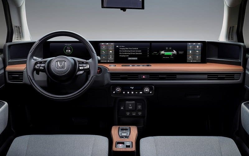 Tablero y volante de automóvil modernos con pantalla digital y detalles de madera, vistos desde los asientos delanteros.