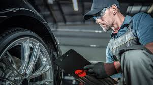 Mecánico inspeccionando una rueda de coche con una tableta en un taller, con guantes y gorra.