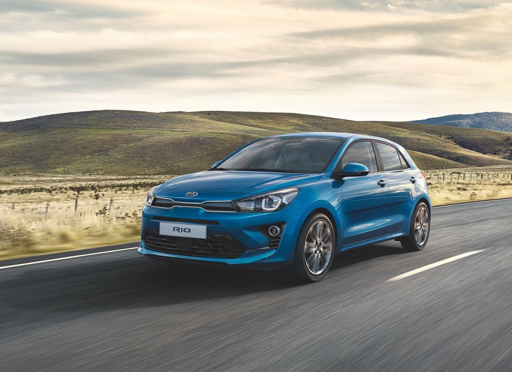 Un coche compacto azul circula por una carretera rural con colinas al fondo.