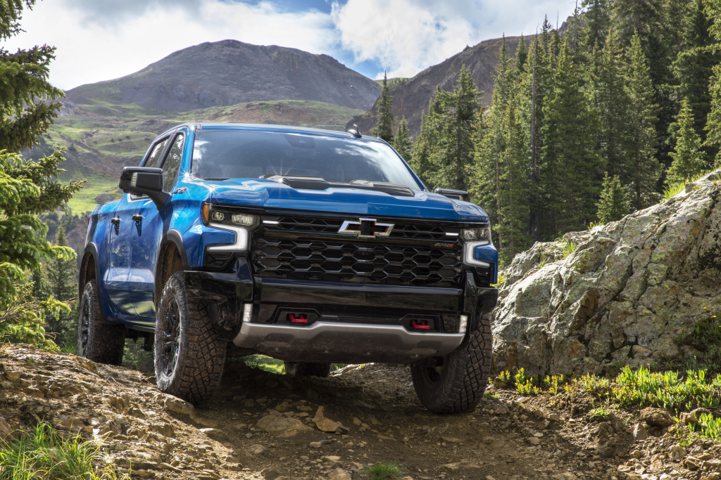 Camioneta azul en un sendero de montaña accidentado con árboles y terreno rocoso.