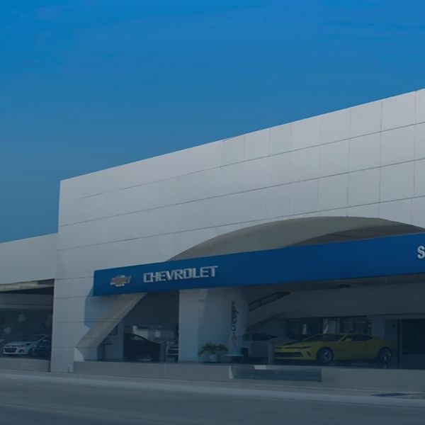 Concesionario Chevrolet con toldo azul y una moderna fachada blanca bajo un cielo azul despejado.