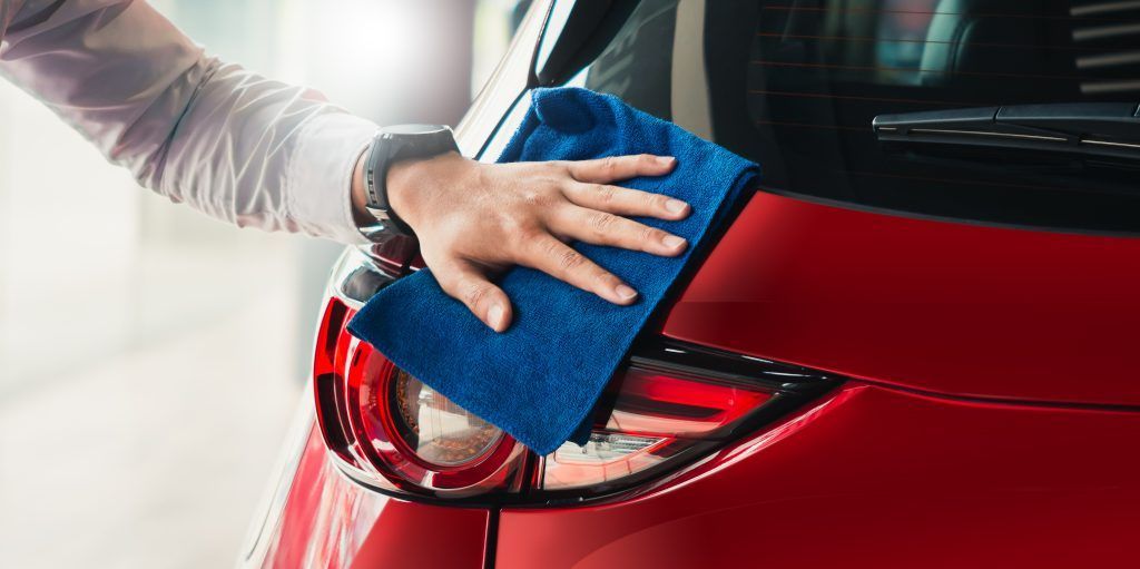 Limpiar a mano la luz trasera de un coche rojo con un paño azul.