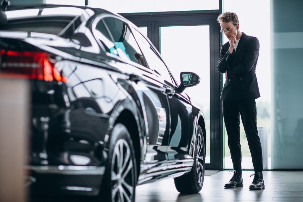 Un hombre con traje negro está de pie junto a un coche negro brillante en una luminosa sala de exposición