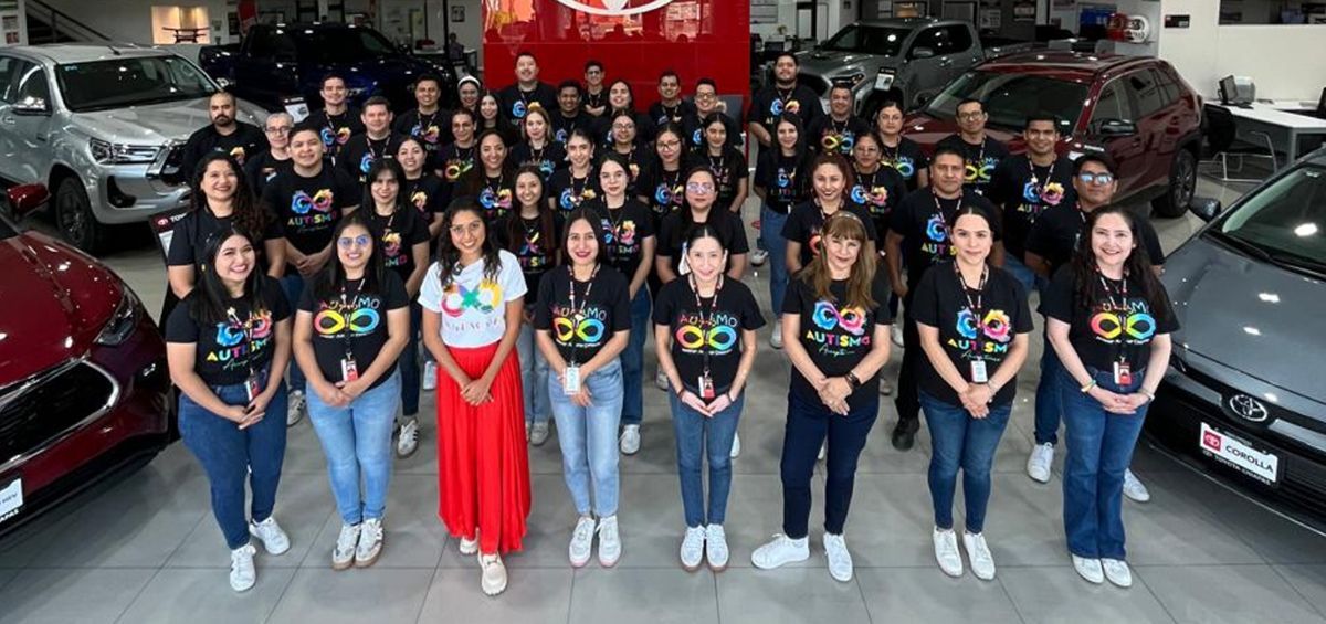Un grupo numeroso posando en una sala de exposición de coches, varios de ellos con camisetas negras iguales