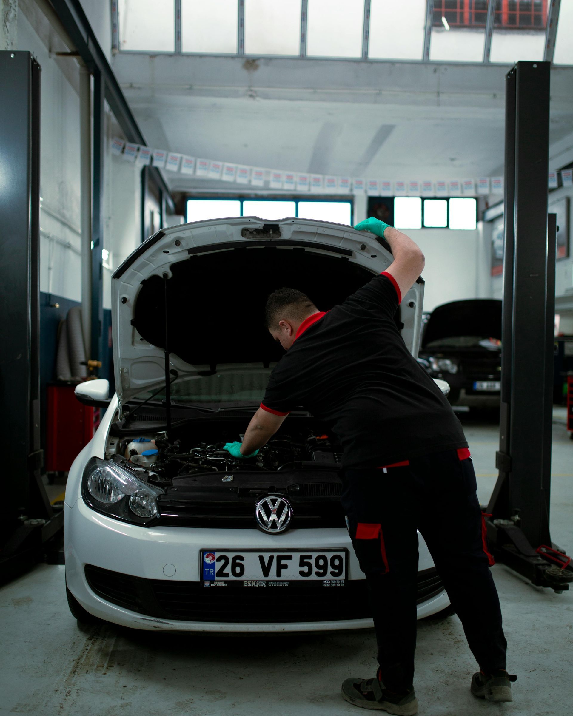 Mecánico trabajando bajo el capó de un Volkswagen negro en un taller mecánico.