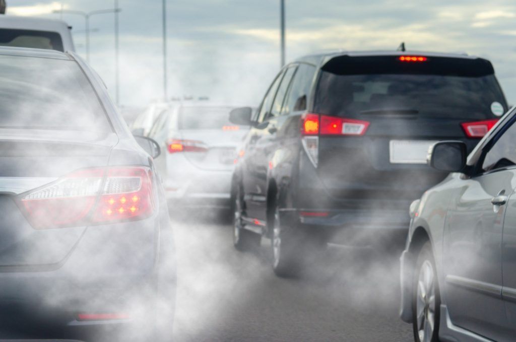 Coches en tráfico denso, cada uno con humo de escape visible en una carretera fría.
