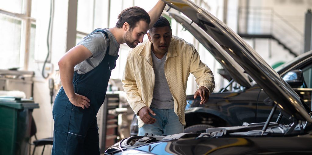 Dos mecánicos inspeccionando el motor de un coche en un taller, con el capó abierto.