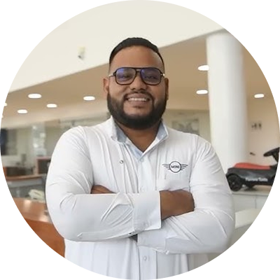Un hombre con camisa blanca y gafas sonríe con los brazos cruzados en el vestíbulo de una oficina muy iluminada.