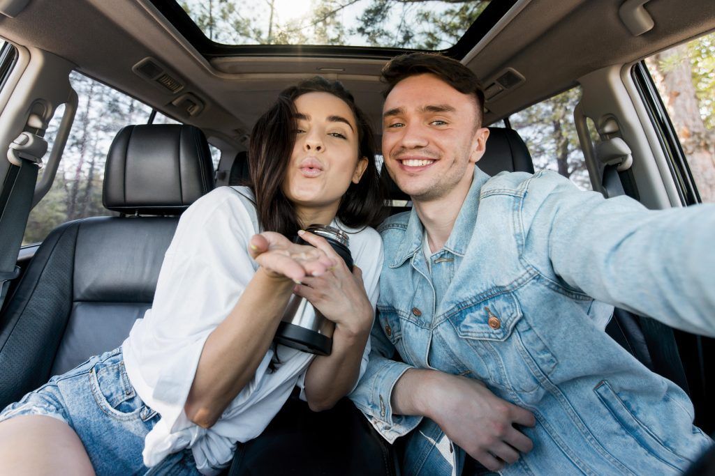 Dos personas sonriendo y tomándose una selfie dentro de un auto con techo corredizo.