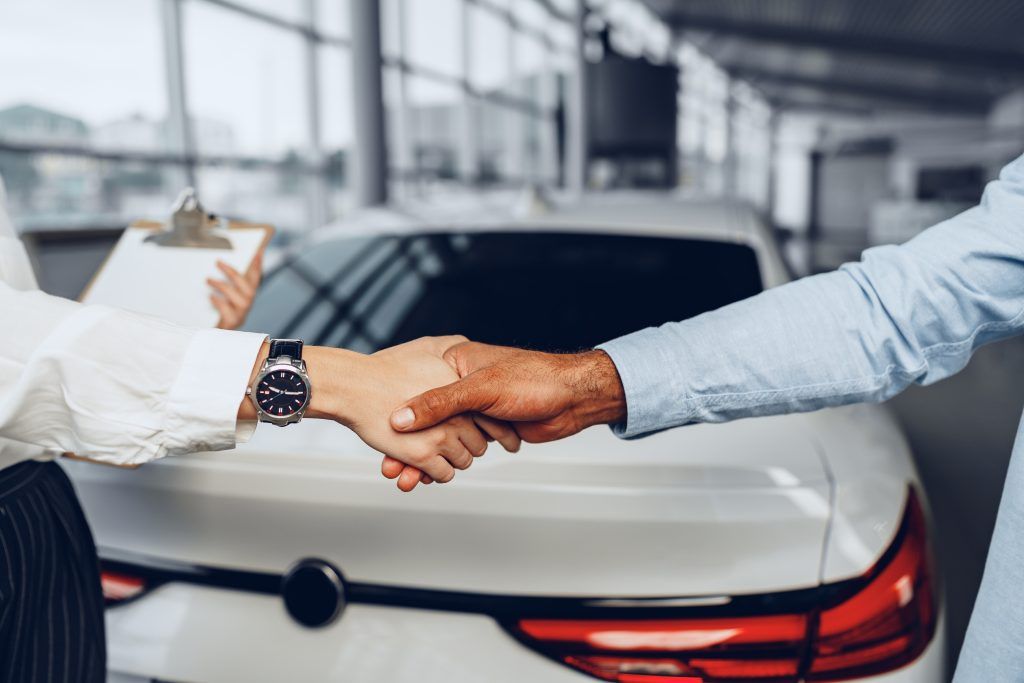 Dos personas se dan la mano frente a un coche blanco en la sala de exposición de un concesionario.