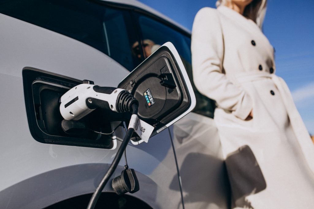 Un coche eléctrico cargándose en una estación junto a una persona con bata blanca.