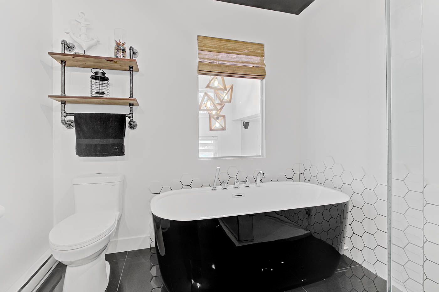 Salle de bains moderne en noir et blanc, avec baignoire îlot, toilettes, étagères et petite fenêtre