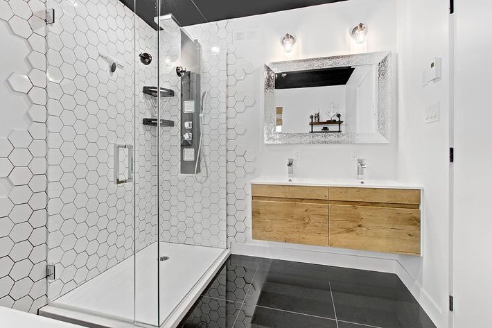 Salle de bains moderne blanche avec douche vitrée, carrelage hexagonal, meuble vasque en bois et grand miroir