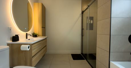 Salle de bains moderne avec meuble-lavabo suspendu en bois, miroir ovale éclairé, douche vitrée et baignoire.