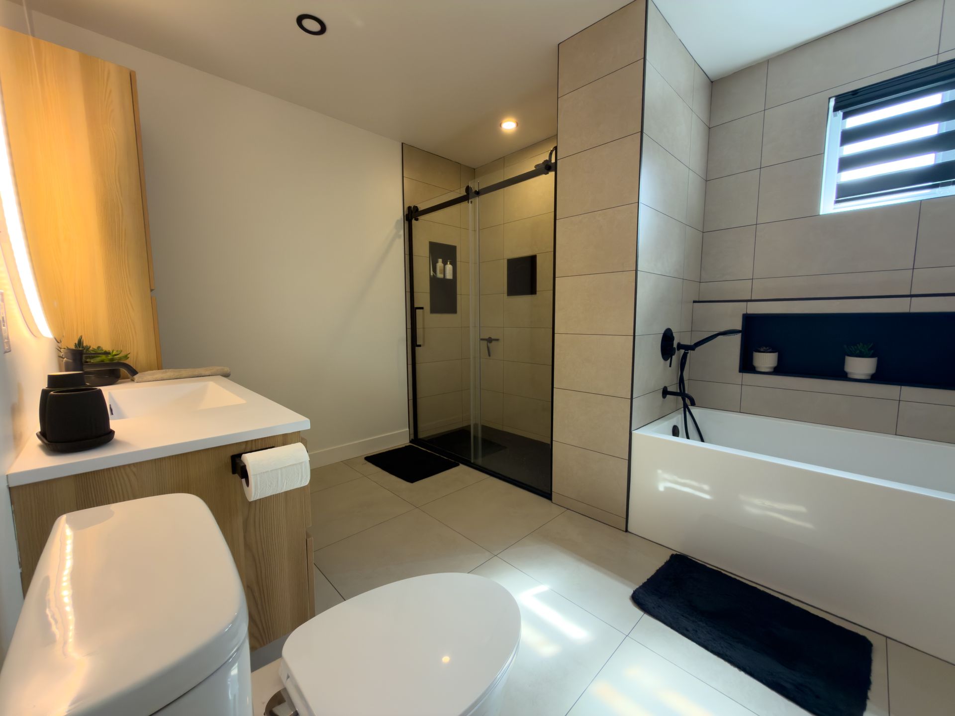 Salle de bains moderne avec baignoire, douche vitrée, équipements sanitaires blancs et murs carrelés beiges
