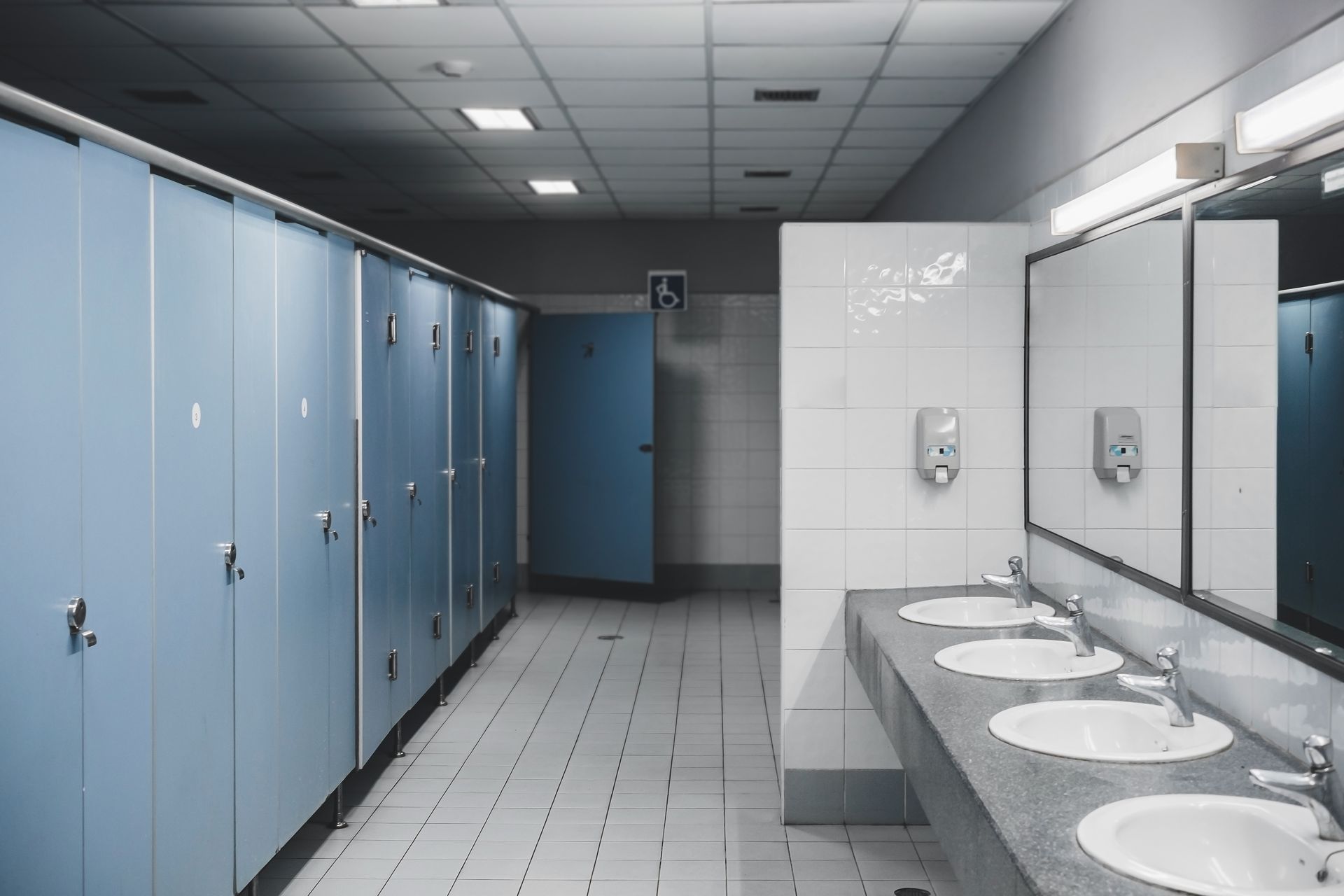 Public restroom with blue stalls, sinks, and mirrors. Tiles and overhead lighting.