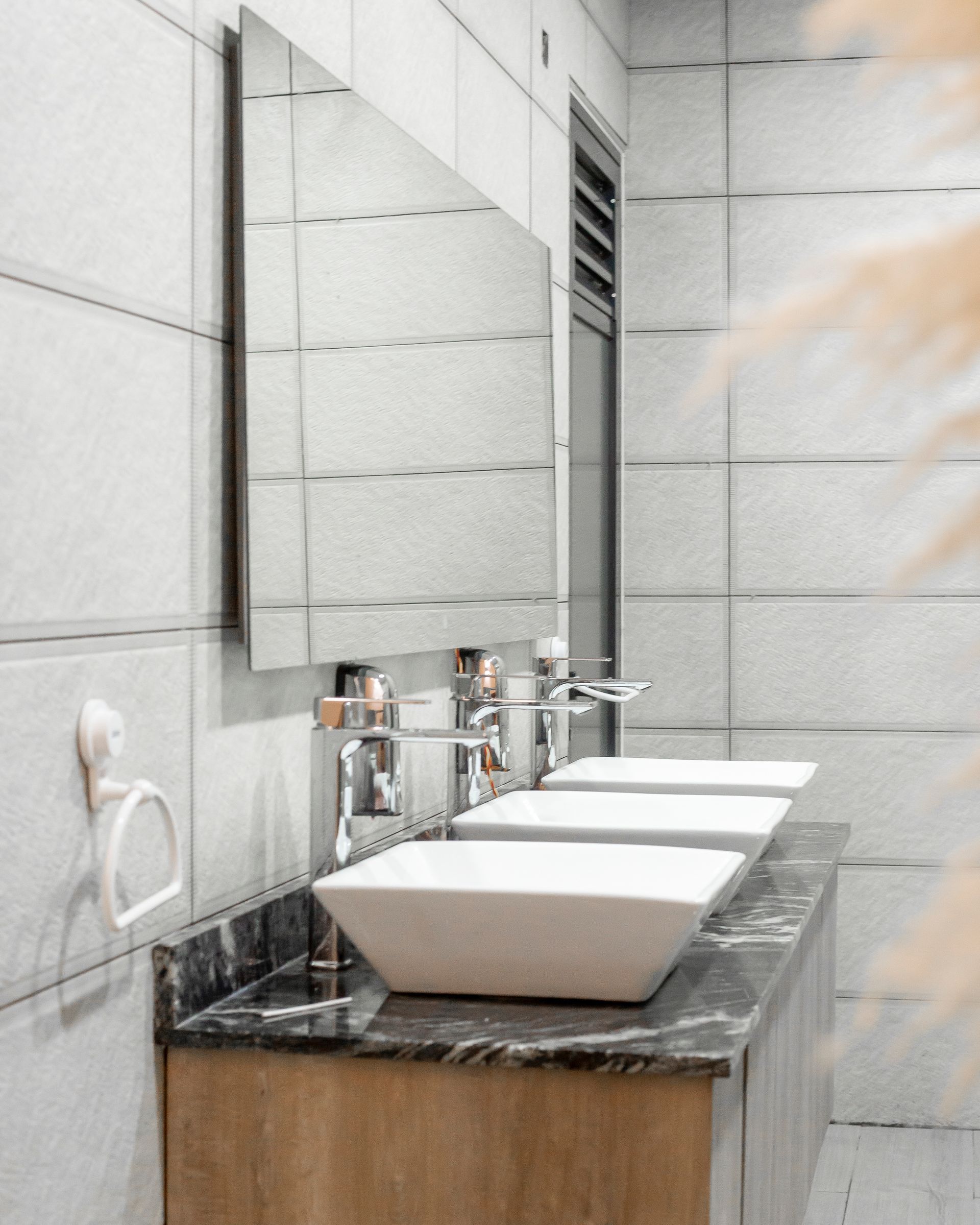 Bathroom vanity with three sinks, a large mirror, and light-colored tiles.