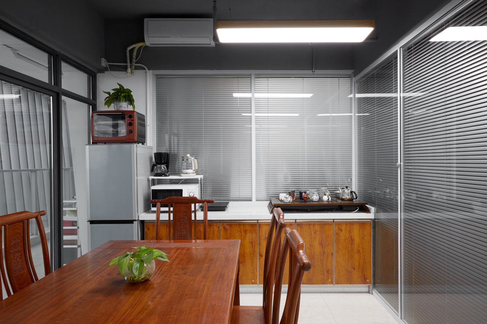 A dining room with a wooden table, chairs, and a kitchenette featuring a refrigerator, microwave, and wooden cabinets.