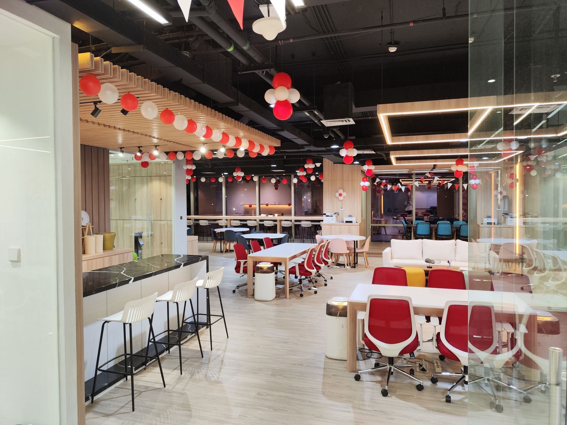 Modern office breakroom with a bar counter, multiple tables, red chairs, and festive hanging decorations.