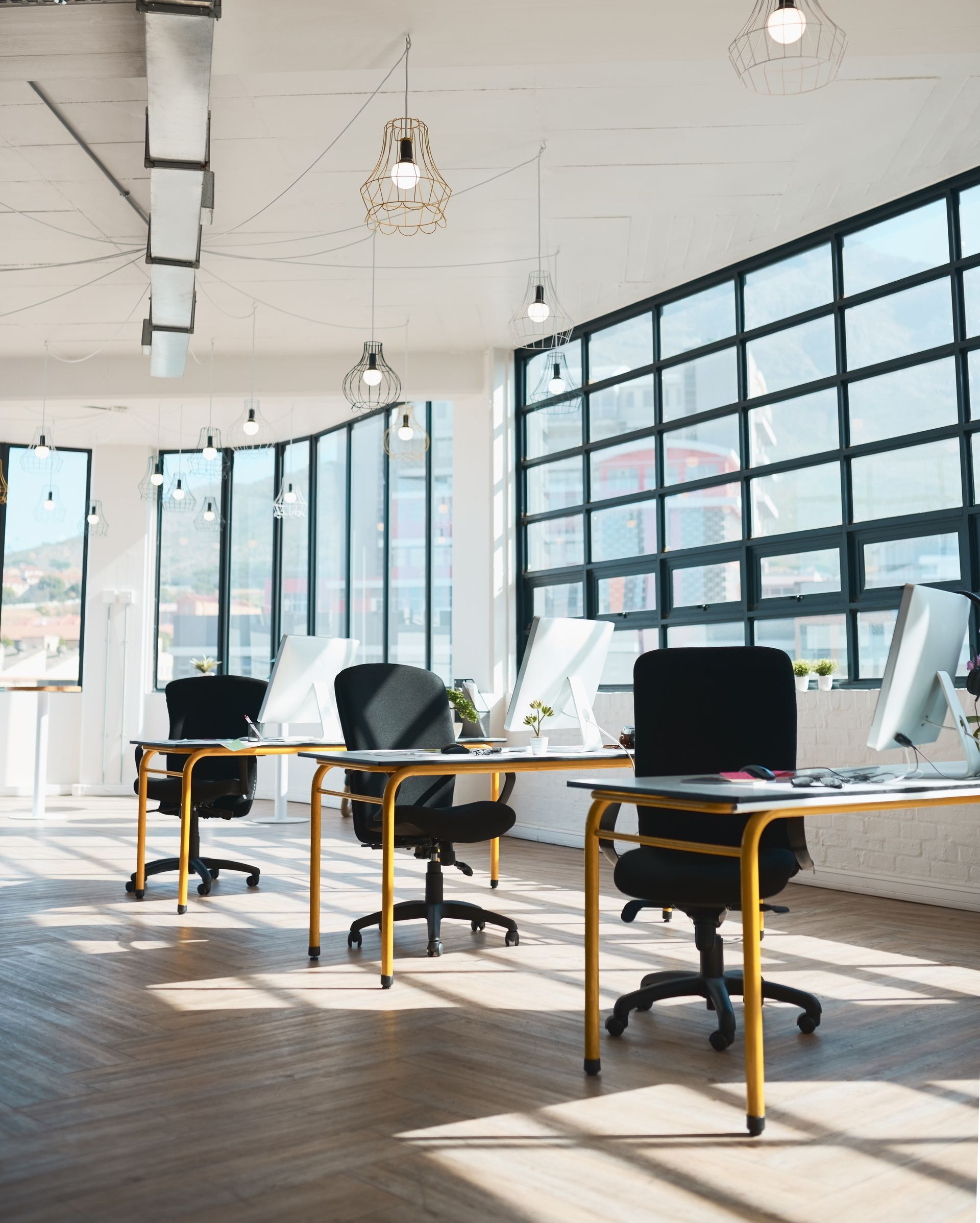 Modern open office with desks, black chairs, and large sunlit windows.