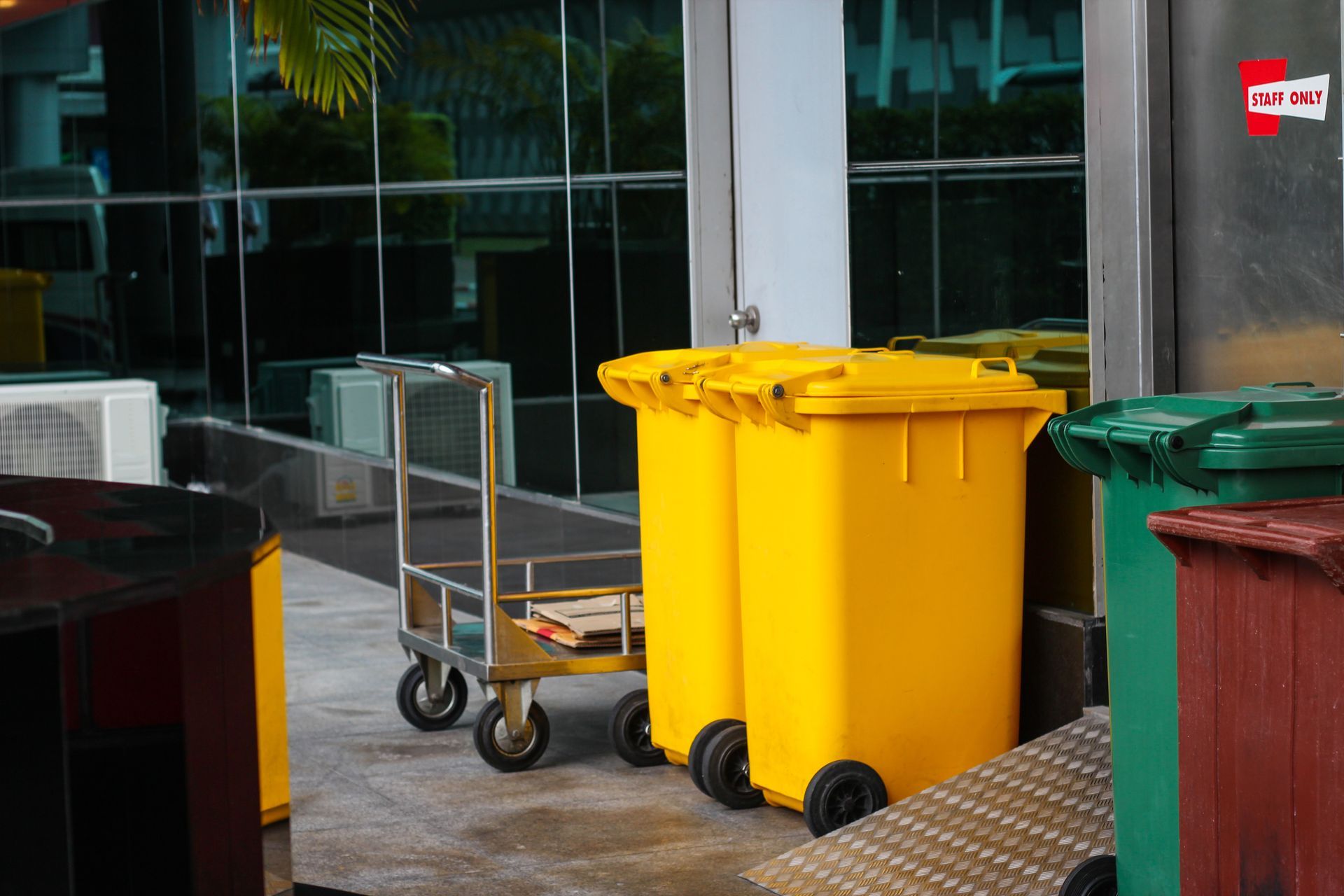Yellow and green trash bins outside a building next to a metal cart.