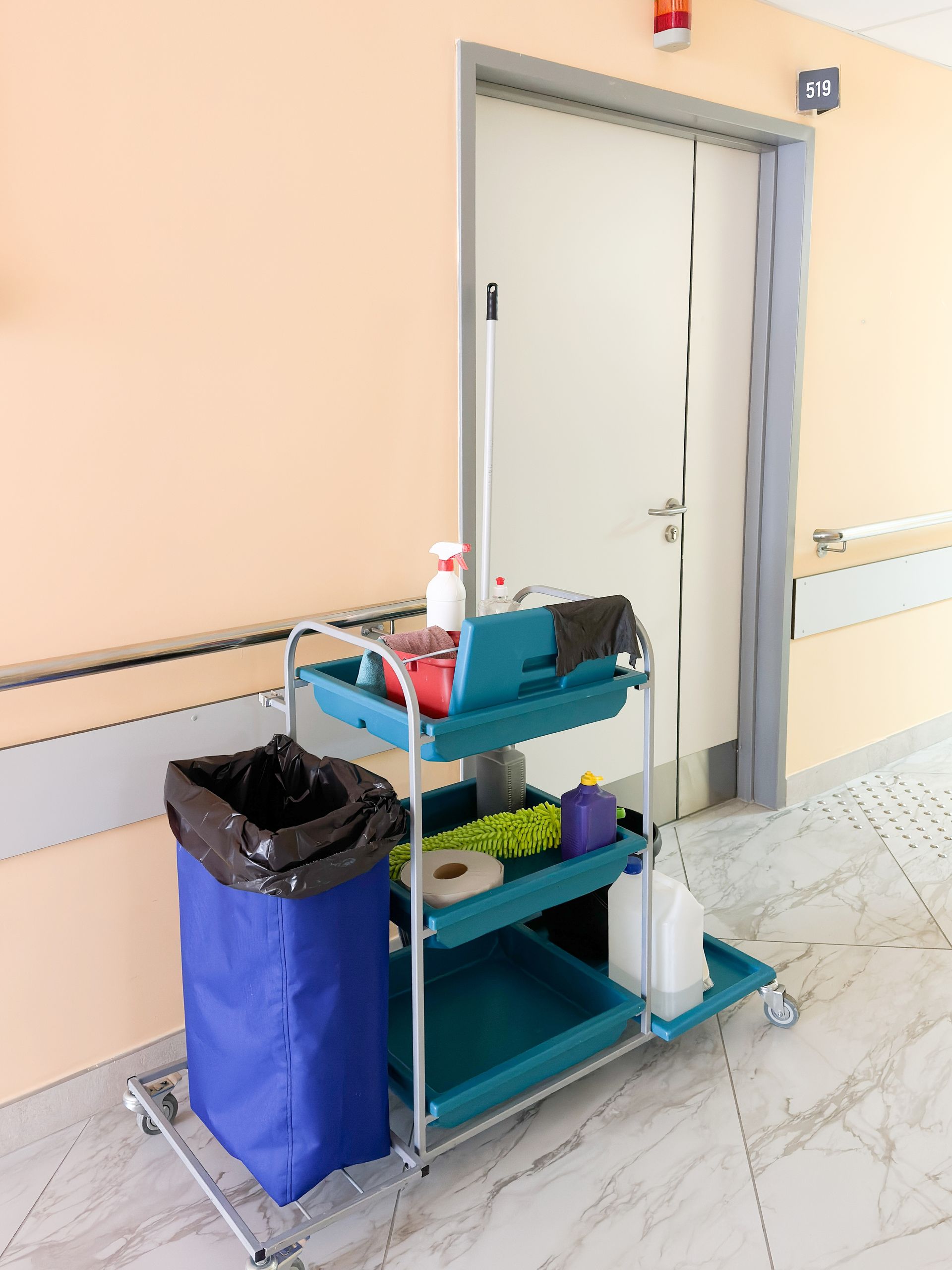 Cleaning cart with supplies beside a doorway in a hallway.