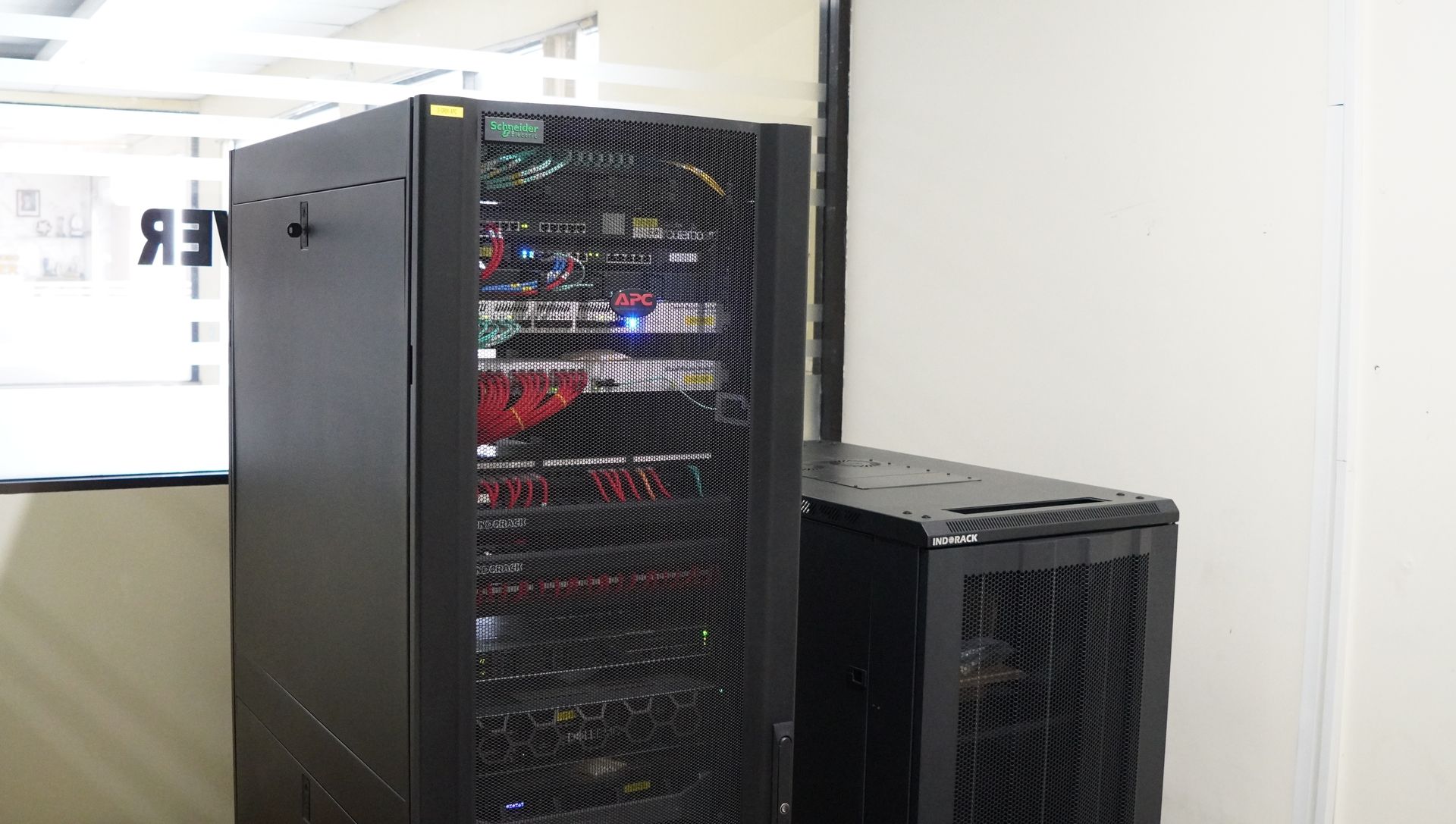 Two black server racks standing side by side in a room with white walls and a window.