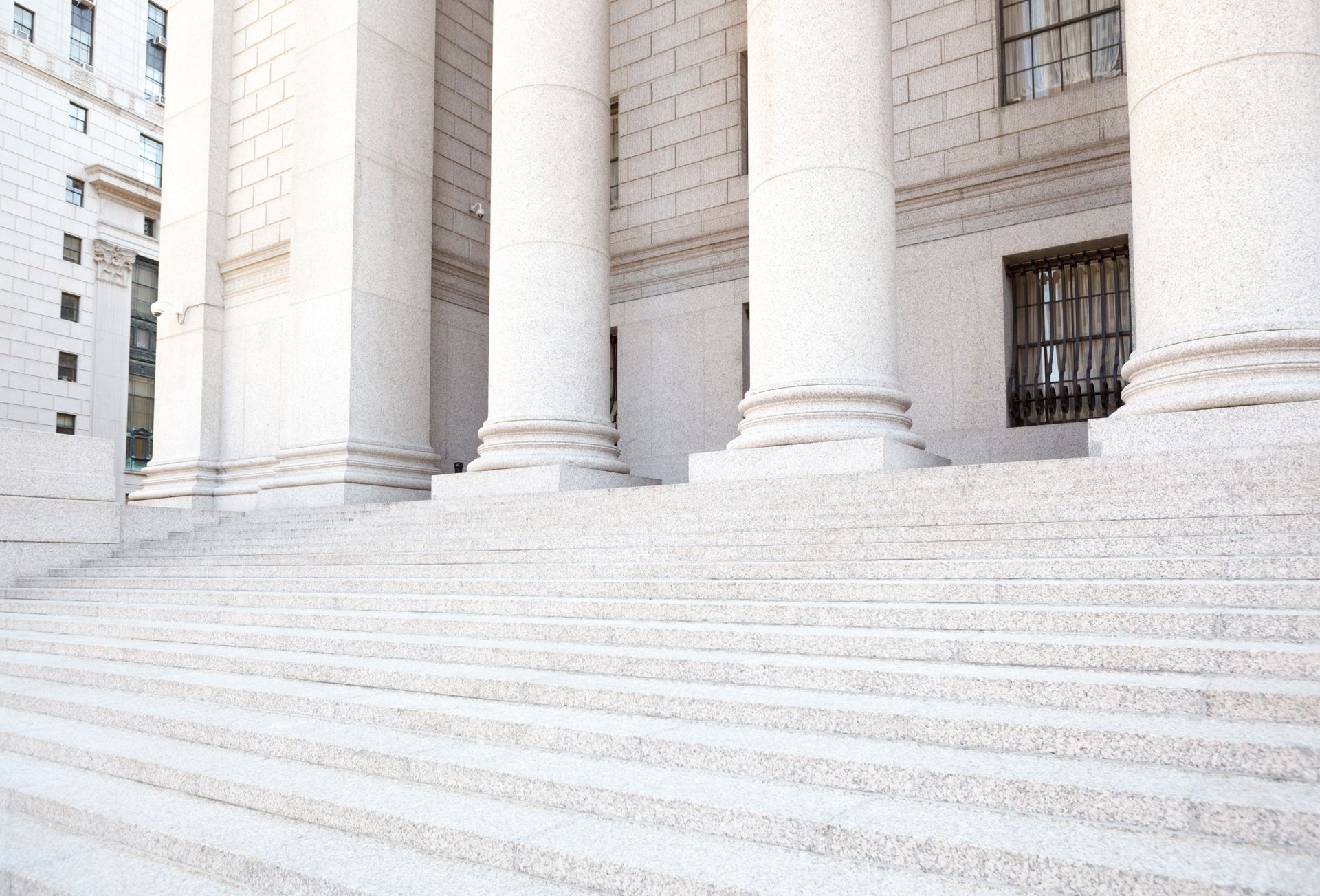 Large stone columns stand atop a long, wide flight of stairs leading to the entrance of a classical, light-colored building.