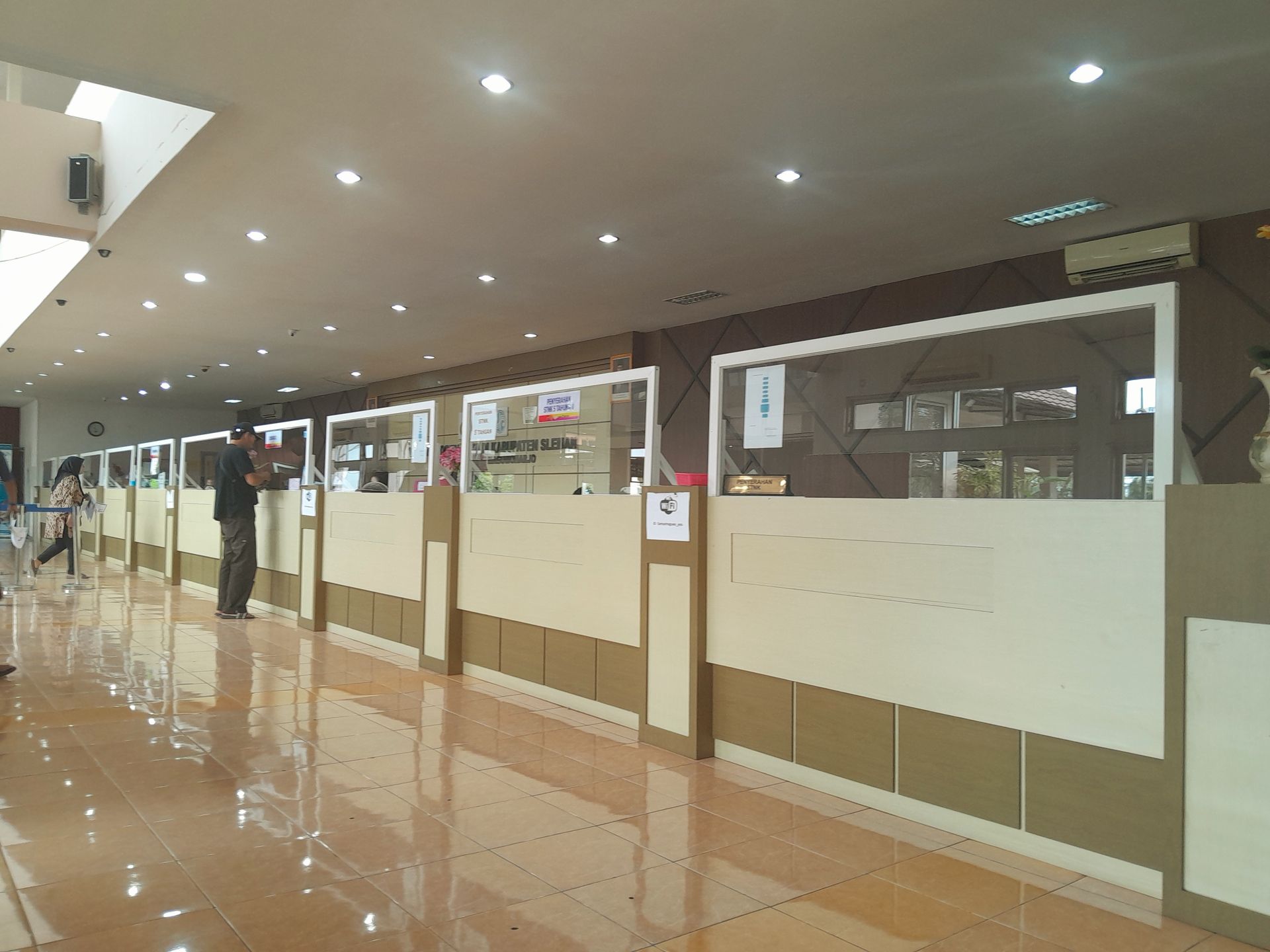 Interior view of a customer service counter with multiple stations featuring glass partitions and light-toned panels.