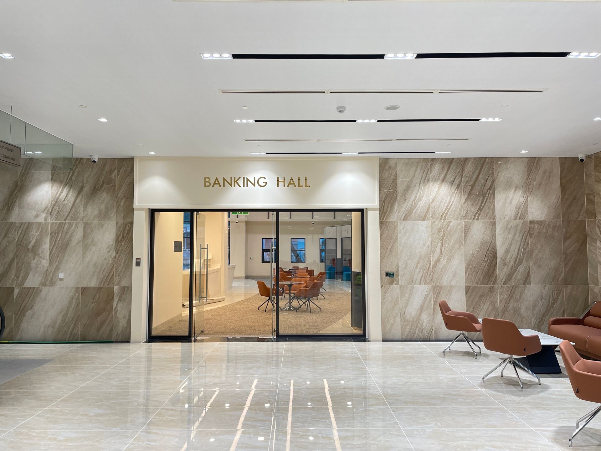Entrance to a Banking Hall featuring tan marble walls, polished floors, and modern brown swivel chairs in the lobby.