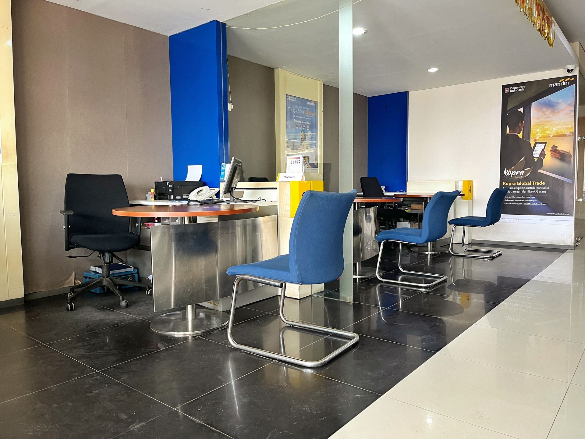 A brightly lit office space featuring rows of desks with blue chairs and a large travel advertisement poster on the wall.