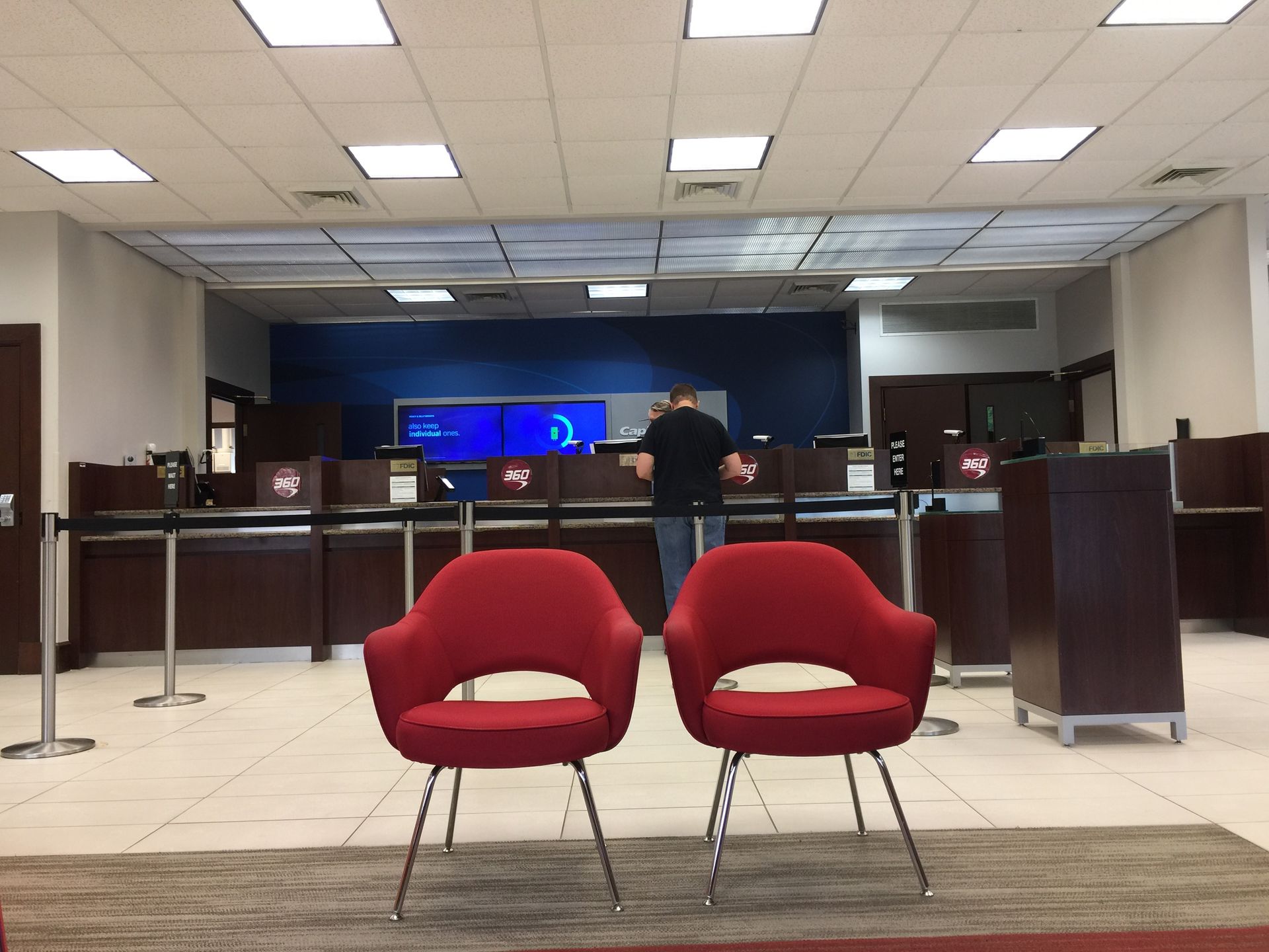 Two red chairs in the foreground of a bank lobby with a teller counter and a person in the background.