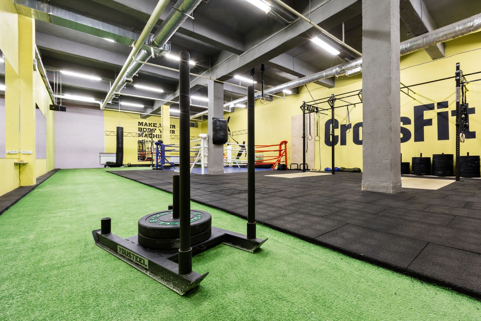 A CrossFit gym with a turf track, a loaded prowler sled, and black rubber flooring under yellow walls.