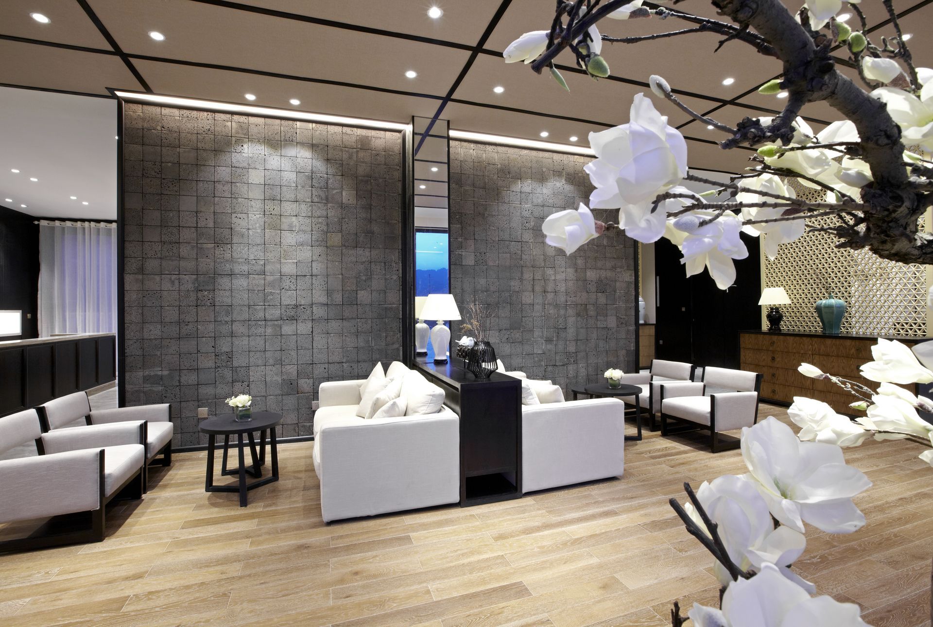 Elegant modern lounge with white furniture, textured screens, and floral accents.