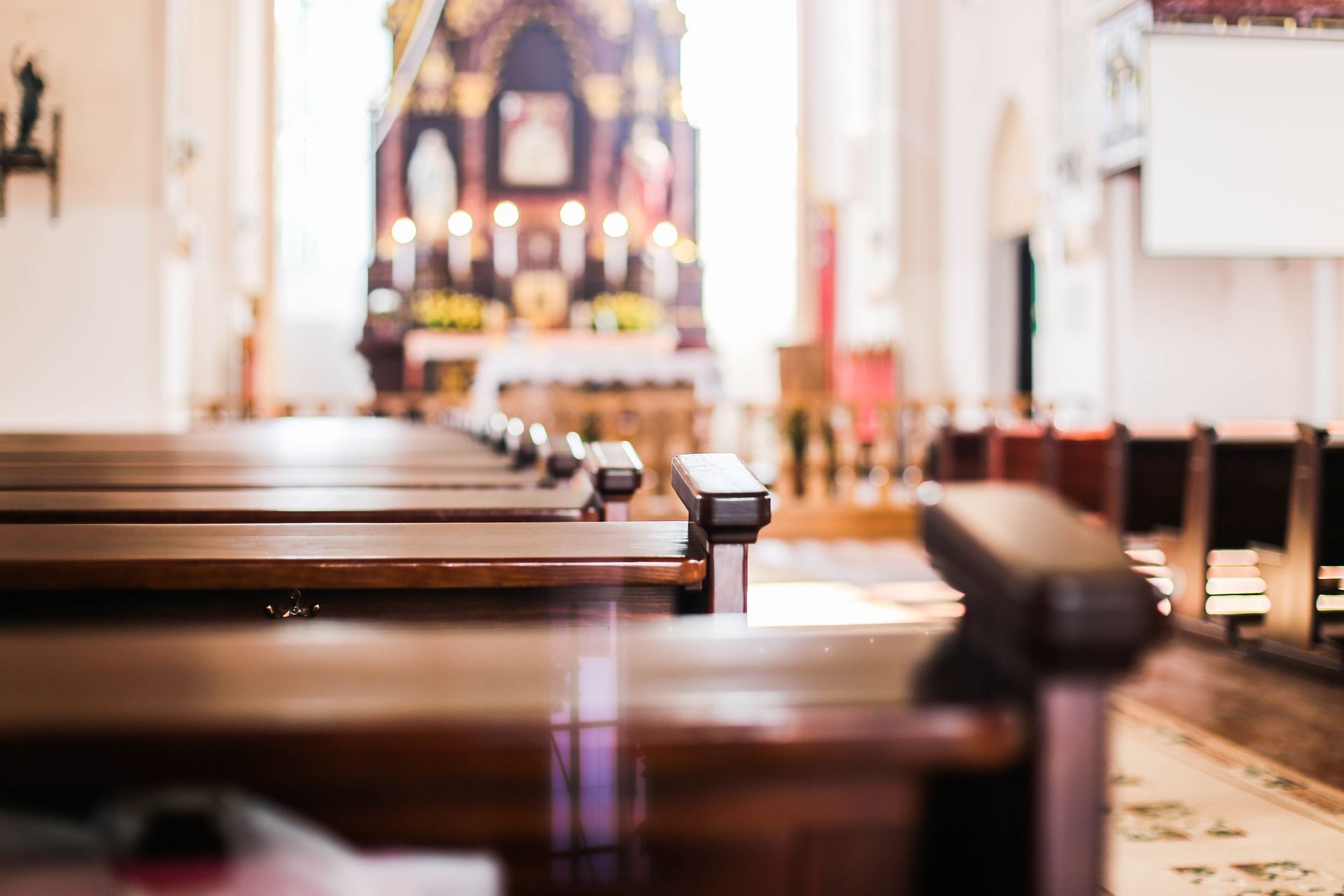Wooden pews in the foreground focus toward the altar of a blurred church interior.