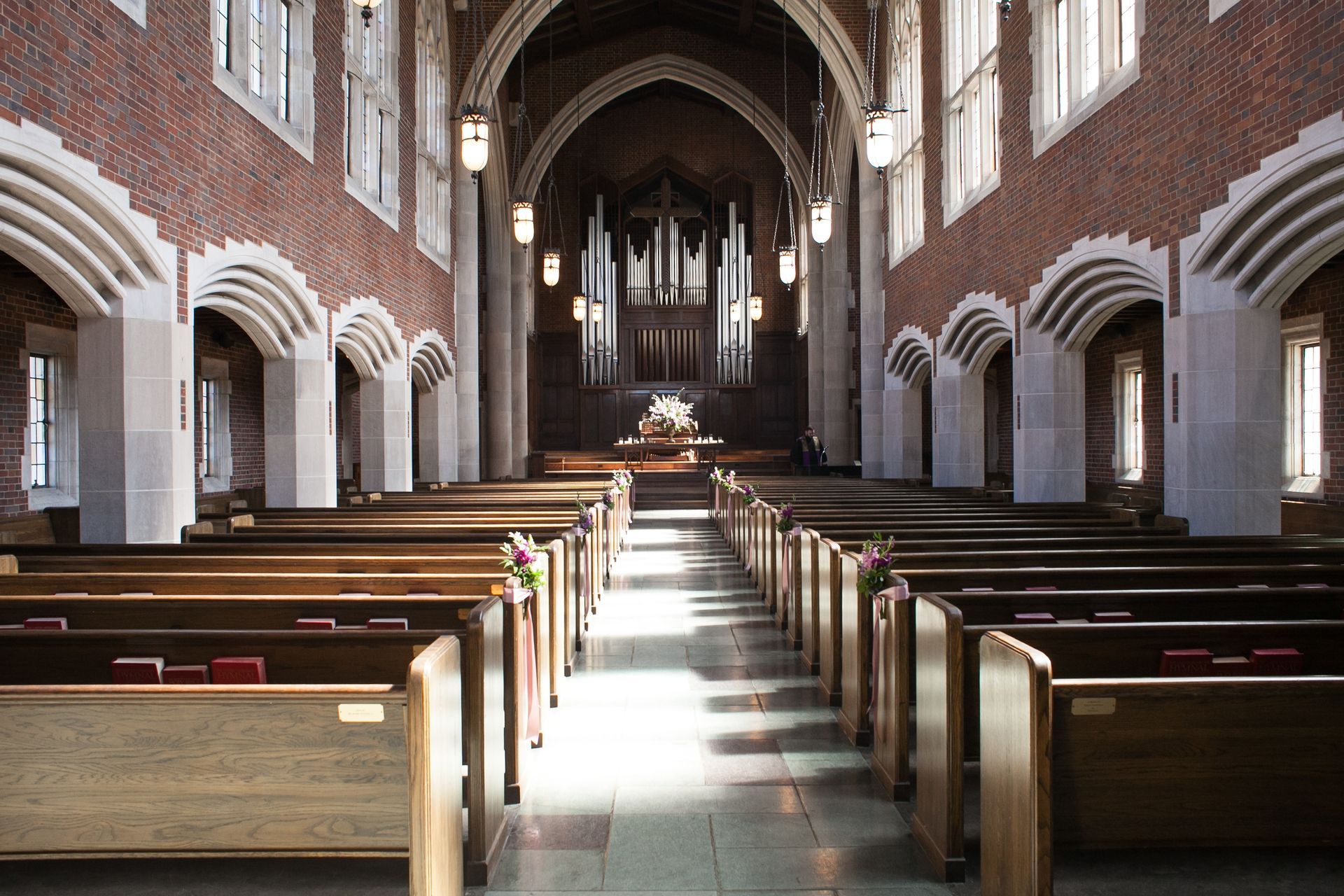 Interior of a church with wooden pews, arched windows, and a pipe organ at the altar.